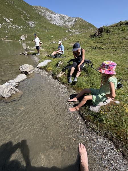 This photo captures a serene summer day at Courchevel, where several people are enjoying the tranquil waters of a mountain lake